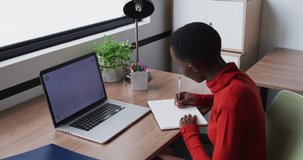 African american businesswoman writing and smiling, on video call using laptop, copy space on screen. work at an independent creative business.