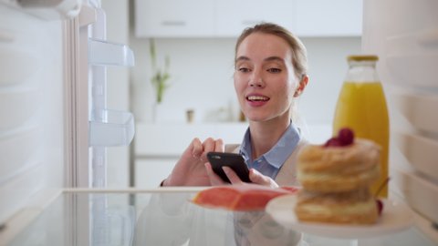 Woman in suit looks into an empty refrigerator, but the problem can be solved! Online ordering of goods from the supermarket. Animation of the appearance of goods. View from inside fridge