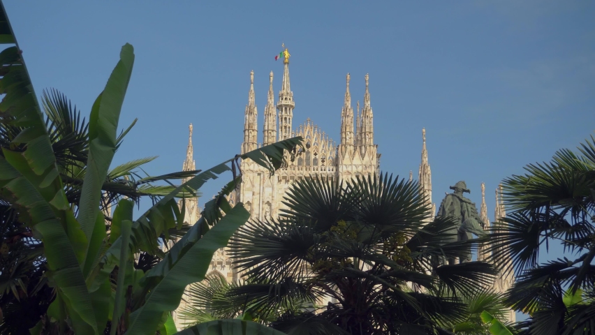 Milan Cathedral and street lamps in front of the Victor Emmanuel II Gallery in Piazza del Duomo. Italy and europe flag. Gothic architecture. Palm trees. Europe Milan Italy May 2021 
