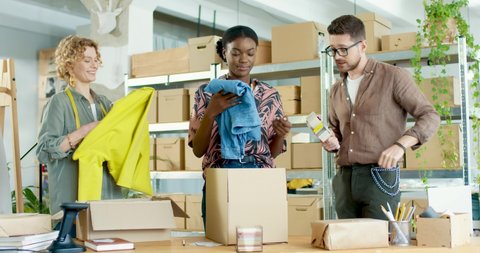 Busy multi-ethnic young joyful male and female clothing store workers working standing in warehouse packing parcels with ordered staff. Fashion industry. Delivery shipment. Clothing business