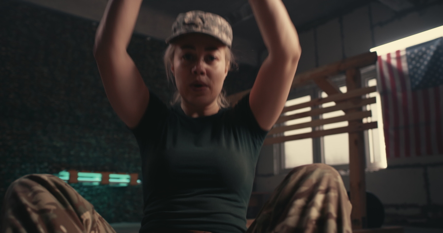 Pan around of strong female soldier doing abdominal crunches near squadmate during intense training in dark gym of USA military base