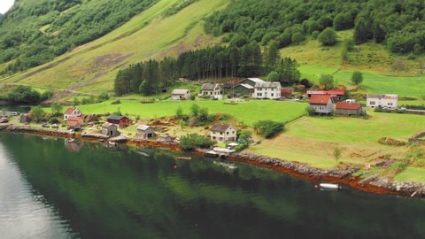 Bird's eye view of the village of in Bakka, Norway. A small village sitting on the coast. Green farm fields and steep, forest-covered mountains. Small tidy houses and a white wooden church.