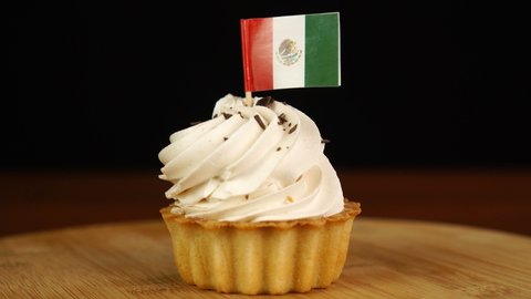 Man places decorative toothpick with flag of Mexico into cream cake. National cuisine