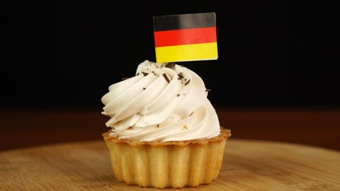 Man places decorative toothpick with flag of Germany into cream cake. National cuisine