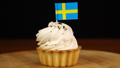 Man places decorative toothpick with flag of Sweden into cream cake. National cuisine