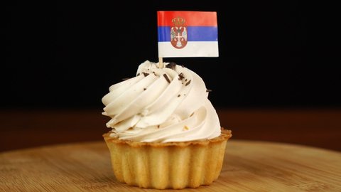 Man places decorative toothpick with flag of Serbia into cream cake. National cuisine