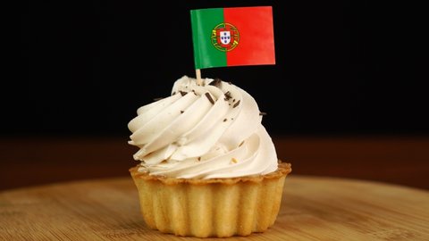 Man places decorative toothpick with flag of Portugal into cream cake. National cuisine
