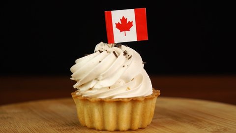 Man places decorative toothpick with flag of Canada into cream cake. National cuisine