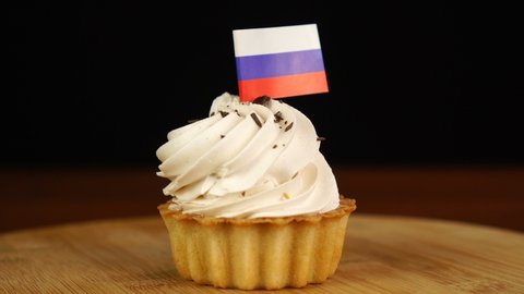 Man places decorative toothpick with flag of Russian Federation into cream cake. National cuisine