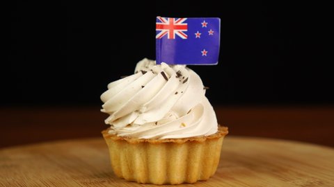 Man places decorative toothpick with flag of New Zealand into cream cake. National cuisine