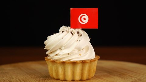 Man places decorative toothpick with flag of Tunisia into cream cake. National cuisine