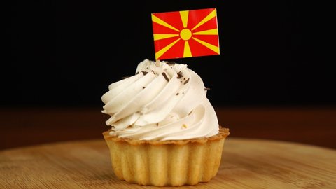 Man places decorative toothpick with flag of Macedonia into cream cake. National cuisine