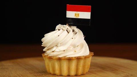 Man places decorative toothpick with flag of Egypt into cream cake. National cuisine