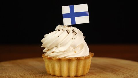 Man places decorative toothpick with flag of Finland into cream cake. National cuisine