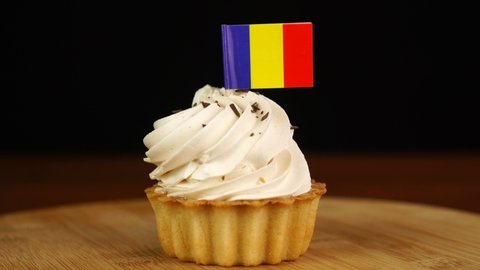 Man places decorative toothpick with flag of Romania into cream cake. National cuisine