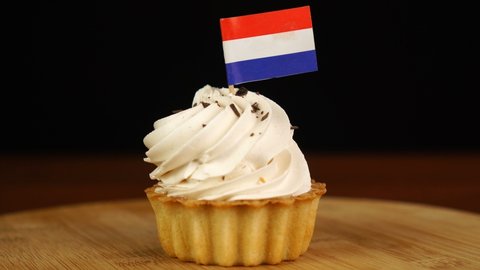 Man places decorative toothpick with flag of Netherlands into cream cake. National cuisine