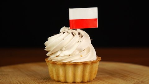 Man places decorative toothpick with flag of Poland into cream cake. National cuisine
