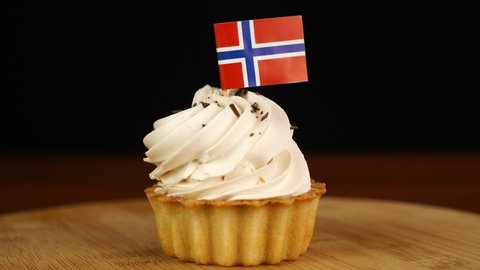 Man places decorative toothpick with flag of Norway into cream cake. National cuisine