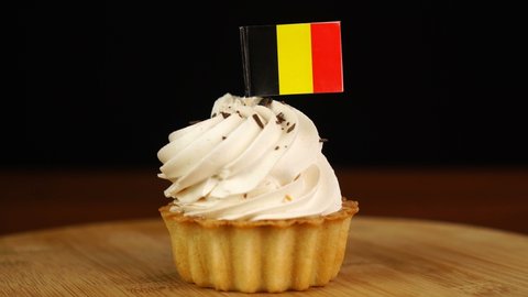 Man places decorative toothpick with flag of Belgium into cream cake. National cuisine