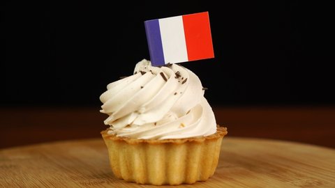 Man places decorative toothpick with flag of France into cream cake. National cuisine