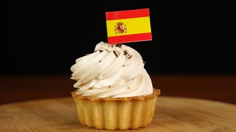 Man places decorative toothpick with flag of Spain into cream cake. National cuisine