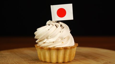 Man places decorative toothpick with flag of Japan into cream cake. National cuisine