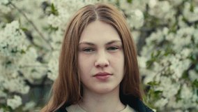 Beautiful young woman in a dark denim jacket in the spring garden in bloom, spring cherry trees blossom, harmony with nature, seasonal spring scene. Slow motion video.