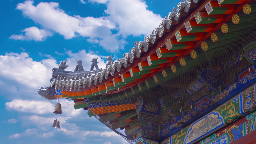 Time lapse of ancient chinese roof with bells under eaves sway on wind, water drops faling from eaves bright blue sky and white cumulus clouds in background. Side view of traditional pagoda tiled roof