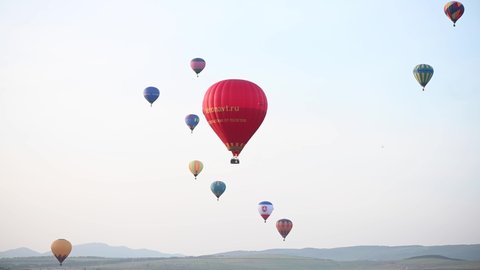 Belogorsk, Russia 01 may 2021: Hot-air balloons open festiva, balloons of different colours fly over rocky mountains, balloons flying on sunset over cloudy sky, 4k HDR footage