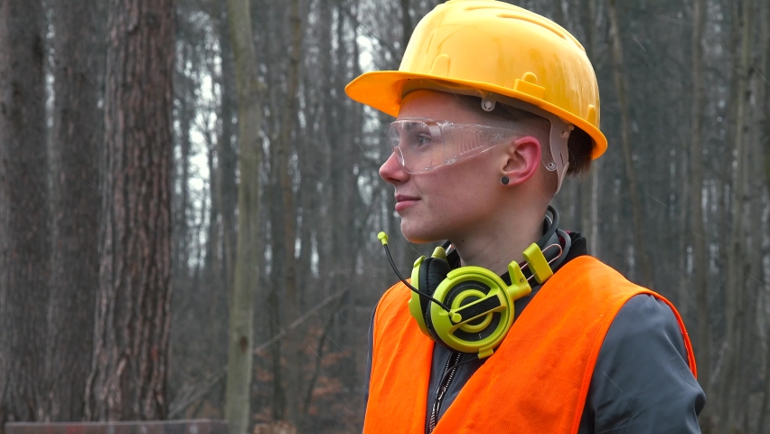 Portrait of a worker in helmet and glasses. Headphones around the neck. Start of new job. Camera movement. The orange vest worker. Royalty-Free Stock Footage #1072057435