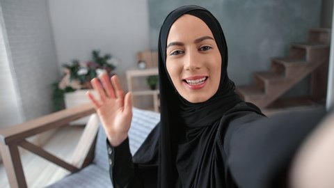 Close up face of Muslim woman in black hijab talking online videoconference call smiling waving hand POV shot. Happy Turkish lady blogger shooting selfie video communicating internet broadcasting