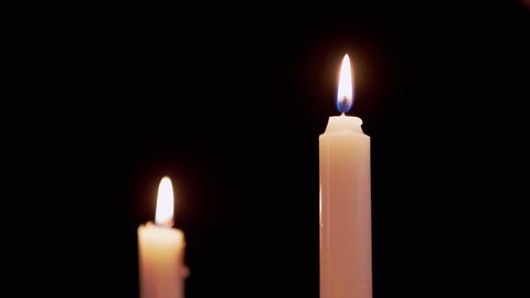 Two White Paraffin Candles Burn with Yellow Fire, on a Black Background. Wax candles with a bright calm flame, fire. Concept of memory, ritual, celebration. Church rites. Slow motion.