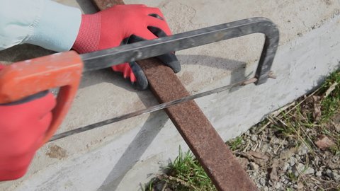 A worker saws off a square metal pipe with a hacksaw.