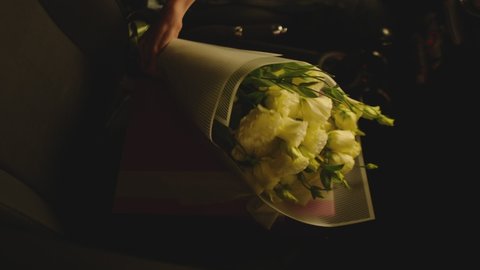 Man putting down white flowers and purple gift box inside car . Male's hand taking beautiful roses or tulips and surprise wrapped present from front seat of car .  Black car interior . Slow motion 
