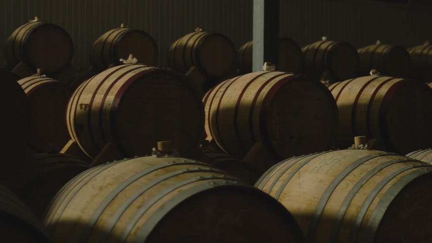 Aged wooden barrels with a wine , brandy or whiskey in a big warehouse . Dolly , gimbal movement a long row of wine barrels at a vintage winery with alcohol . Wine preparation and fermenting process Royalty-Free Stock Footage #1072063264