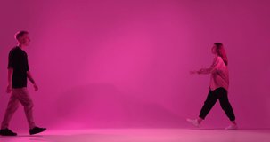 Cool dancing young couple moving in pink neon studio light. Contemporary dance, hip hop dancers performance