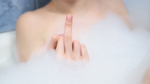 Fuck you sign by woman hand in foam in bath, middle finger sign, closeup view. A sign of aggression, indifference and rejection, rudeness and boorishness.