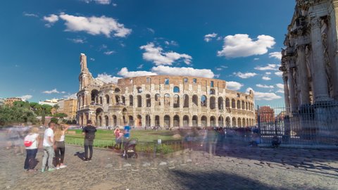 Many tourists visiting The Colosseum or Coliseum timelapse hyperlapse, also known as the Flavian Amphitheatre in Rome, Italy. Green lawn. Blue sky with clouds at sunny day