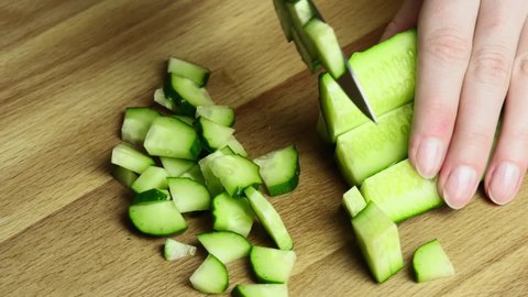 Woman cutting cucumber with knife on a wooden board. slow motion