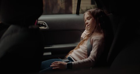 Cute little child girl sleeping on a back seat of a modern SUV while riding through neighborhood. Shot with 2x anamorphic lens