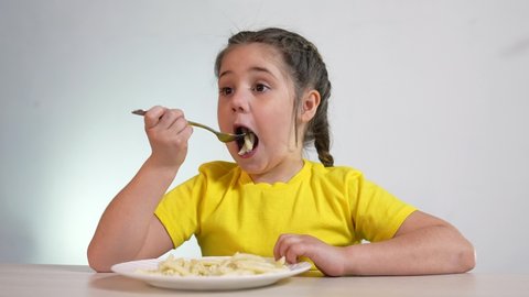 child eating pasta. healthy a food vegetarianism concept. girl child at the table in the kitchen eating indoor pasta. kid eating pasta. little girl at the table eats short spaghetti pasta