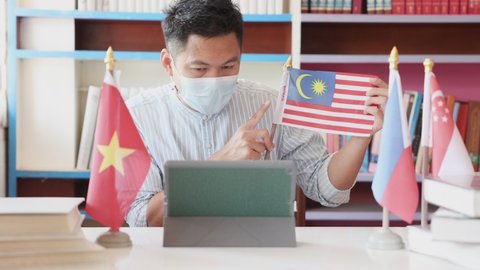 A young teacher wearing a mask teaches online Malaysian flag. Online teaching ideas during detention and safe distances from COVID 19