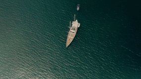 White yacht anchored in blue water near a paradise tropical island. Self-isolation on a boat. Travel business is recovering from the coronavirus pandemic. Drone video top bird eye view.