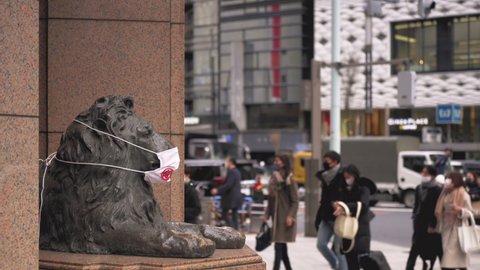 tokyo, japan - january 08 2021: Video of the bronze sculpture of the lion of the Ginza Mitsukoshi store wearing a mask during the coronavirus pandemic with pedestrians walking beside.