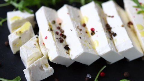 Selective focus. Macro. Sliced feta cheese on a black stone board with spices and olive oil.