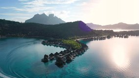 Luxury travel vacation aerial of overwater bungalows resort in coral reef lagoon ocean by beach. Aerial Drone video at sunset paradise getaway Bora Bora, French Polynesia, Tahiti, South Pacific Ocean.