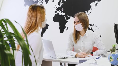 Travel agent having a client in light modern office of tour, choose travel destination on the globe. Assistant speaking in face mask in the travel agency to clients. protection during covid pandemic 