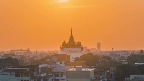 Time lapse Sunset in Bangkok city of Thailand on top of the pagoda Golden mountain, Wat Saket. The Sun falling on and piercing through pagoda's peak under the golden sky in the evening.