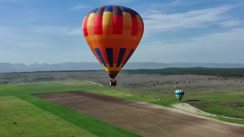 A multicolored hot air balloon with a basket flies against the blue sky. aerial view.  Royalty-Free Stock Footage #1072103960