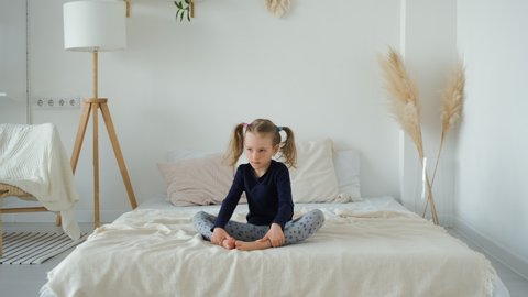 Cute Smiling Little Girl Doing Yoga Exercises while Sitting on a Bed at Home. Slow Motion. Healthy Lifestyle, Sport Practice and Recreation Concept